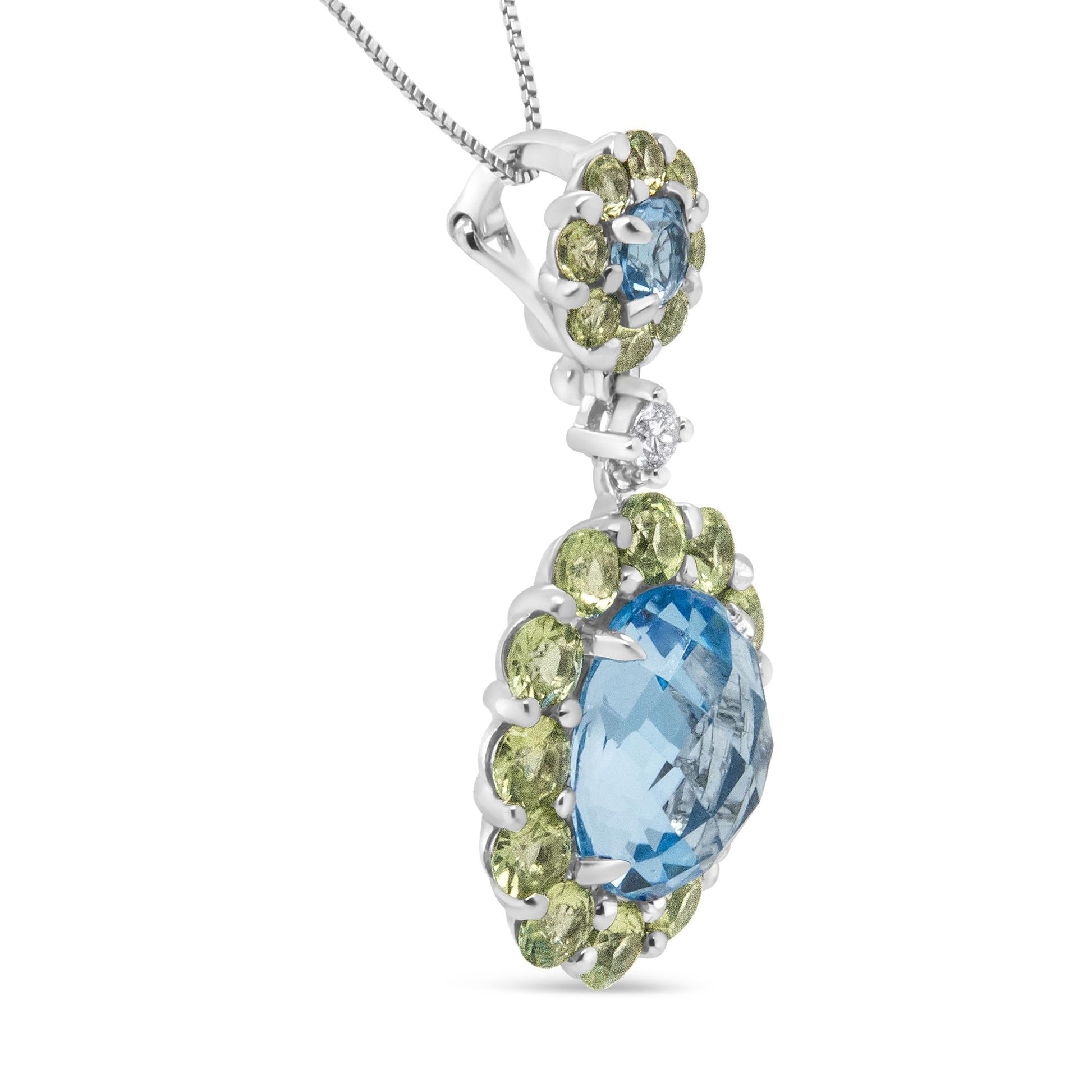 Close-up side view of a white metal necklace pendant featuring one large oval blue gemstone surrounded by multiple small round green gemstones, one small round blue gemstone with surrounding small round green gemstones above it, and a single small round white gemstone connecting the two sections.