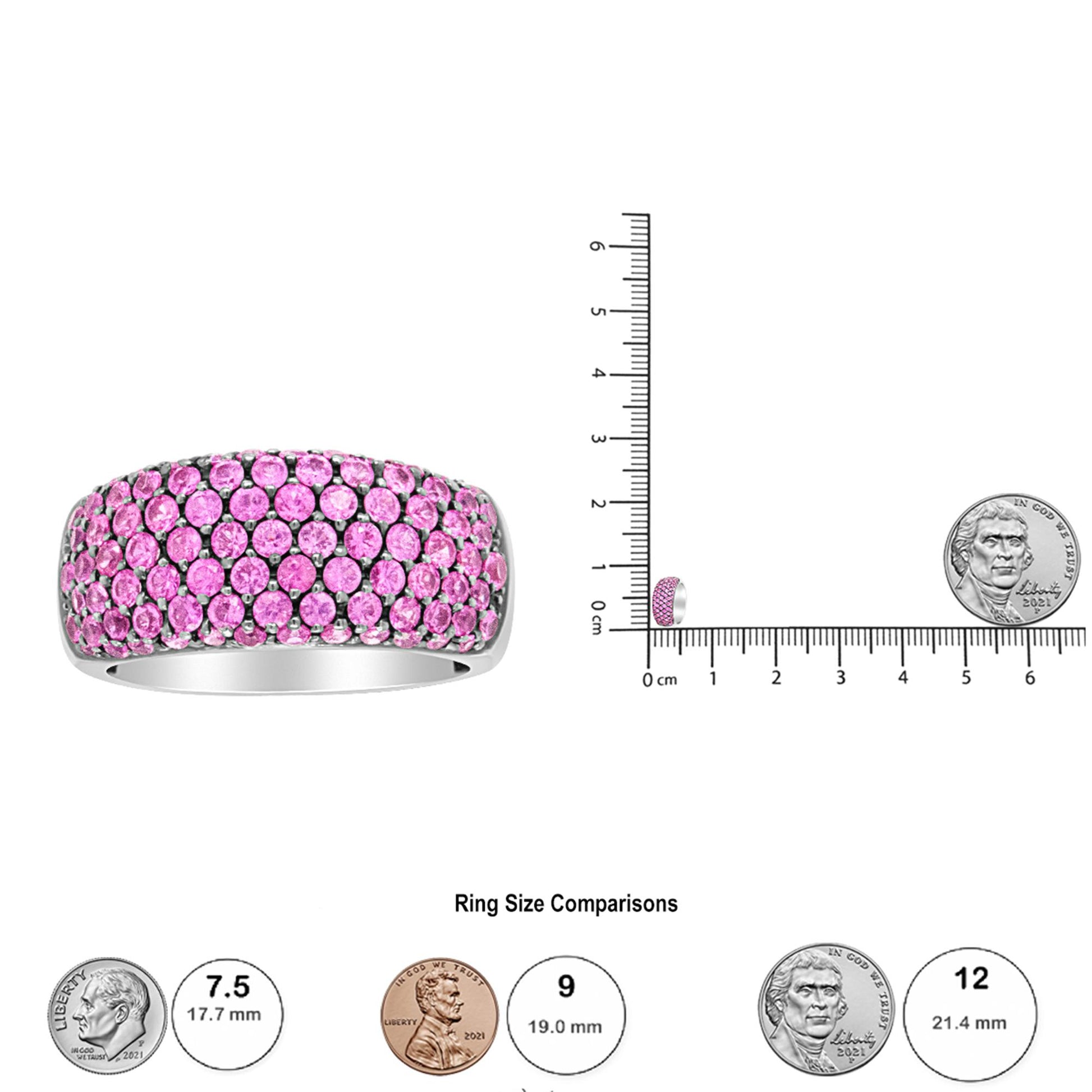 White ring set with multiple round pink gemstones in prong settings, shown from a front angle and displayed on a ruler with coins for size reference.