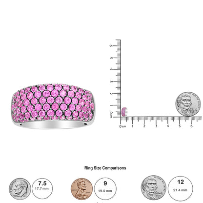 White ring set with multiple round pink gemstones in prong settings, shown from a front angle and displayed on a ruler with coins for size reference.