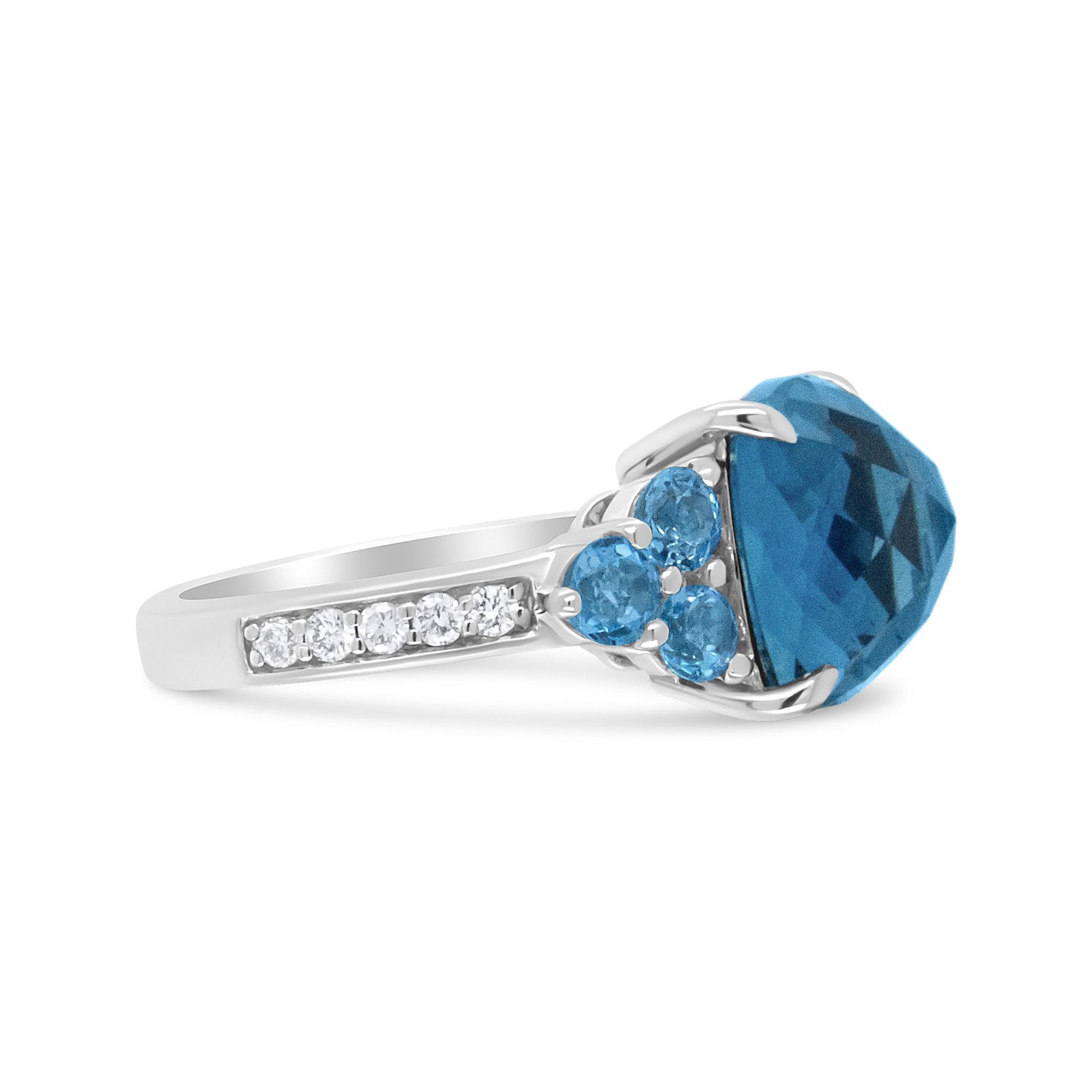 White metal ring with a large blue gemstone center, accented by smaller blue gemstones and a row of white round prong-set gemstones on the band, shown in a side profile angle.