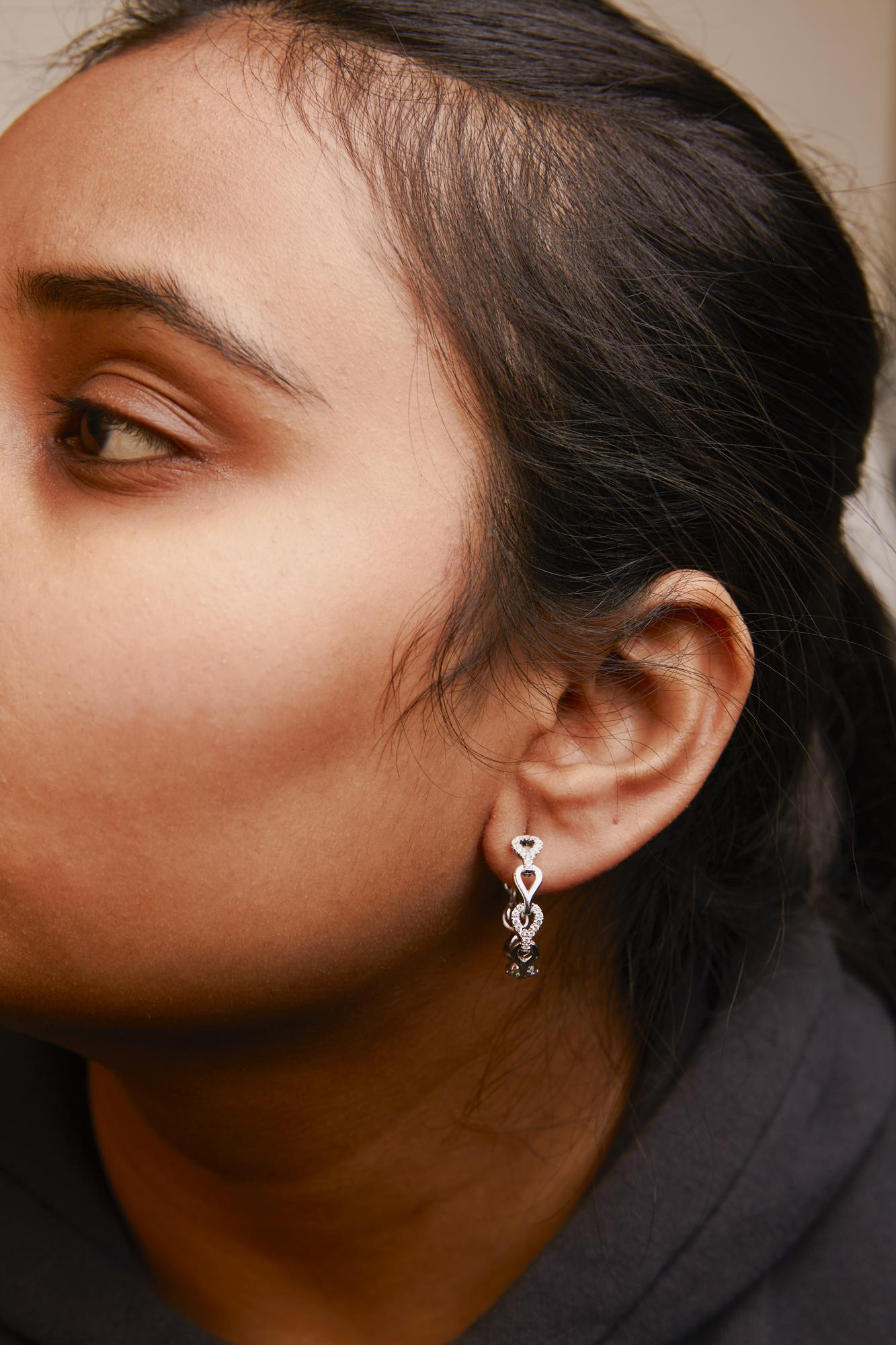 Close-up side view of a model wearing white metal dangle earrings adorned with round white gemstones in prong settings.