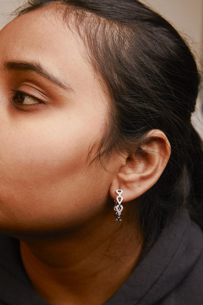 Close-up side view of a model wearing white metal dangle earrings adorned with round white gemstones in prong settings.