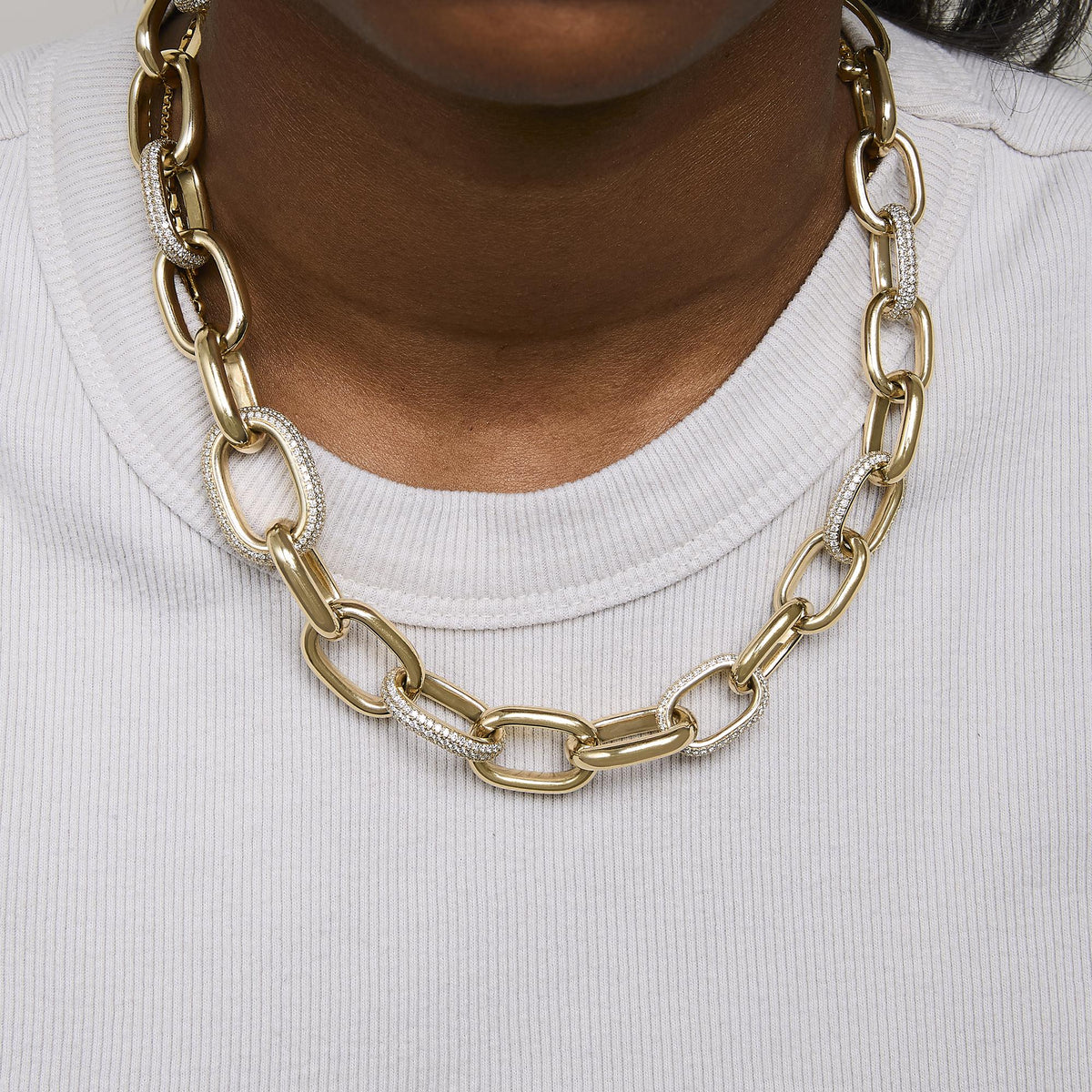 Close-up front view of a model wearing a yellow metal necklace featuring large links, some adorned with white gemstones in a pave setting.