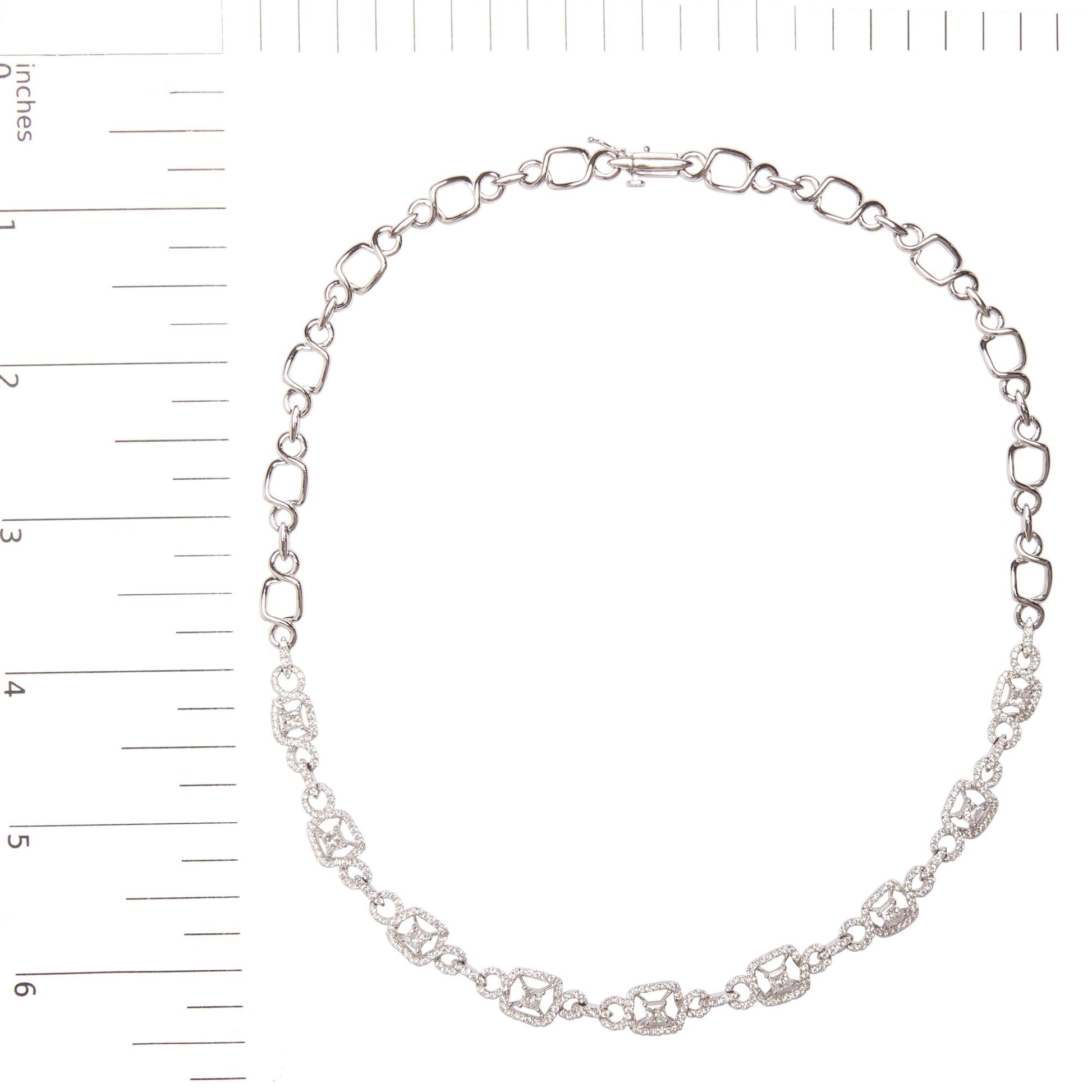 Top-down view of a white metal necklace with alternating geometric links, some adorned with prong-set white princess shape and round gemstones, displayed on a ruler for size reference.