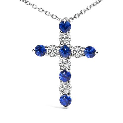 White metal cross-shaped necklace pendant with alternating round white and blue gemstones in prong settings, shown against a white background from a front angle.