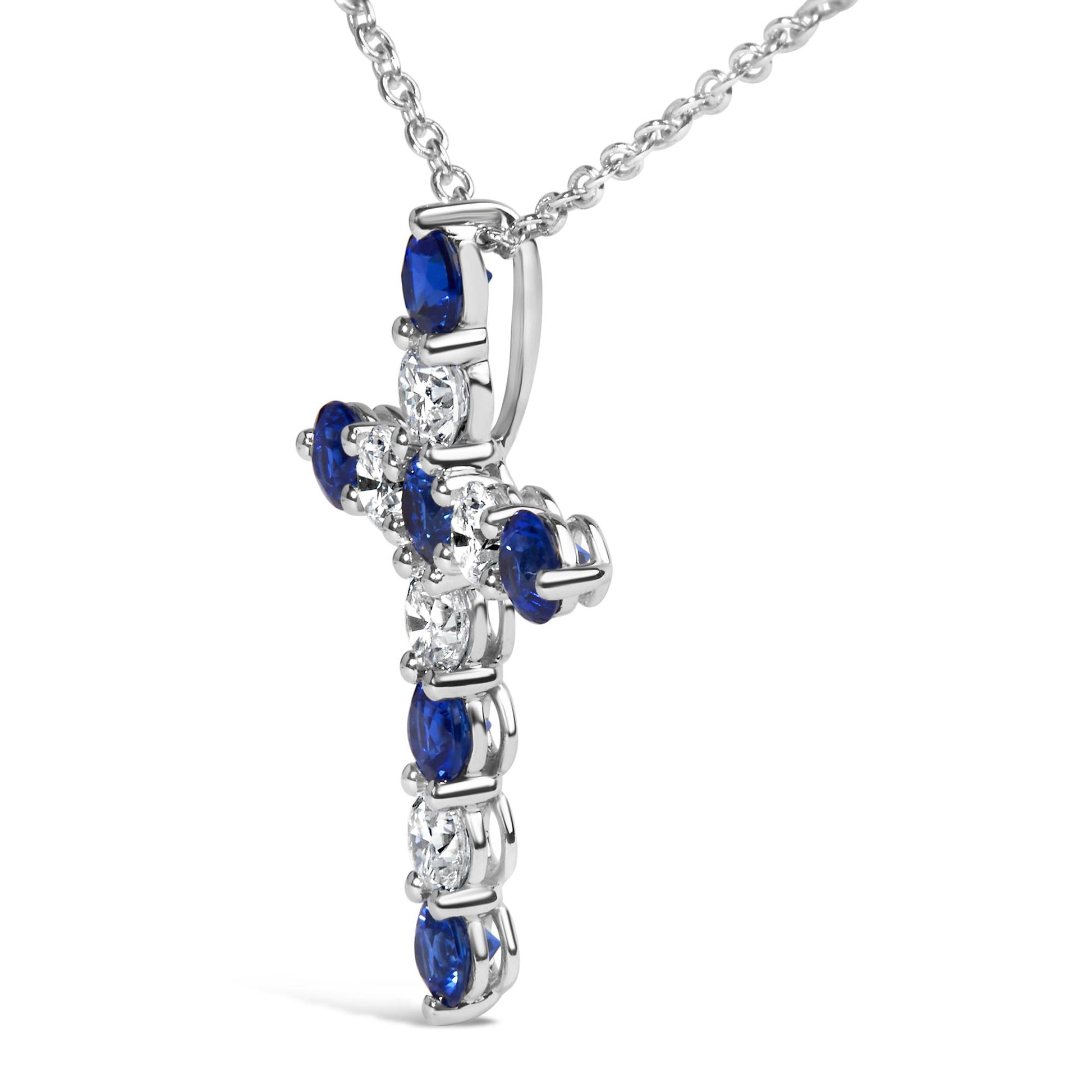 Close-up side angle of a white metal cross-shaped necklace pendant featuring alternating round white and blue gemstones in prong settings on a chain.