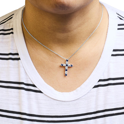 Necklace with a cross-shaped pendant featuring round white and blue gemstones in prong settings on a white metal chain, shown on a model from a front angle.