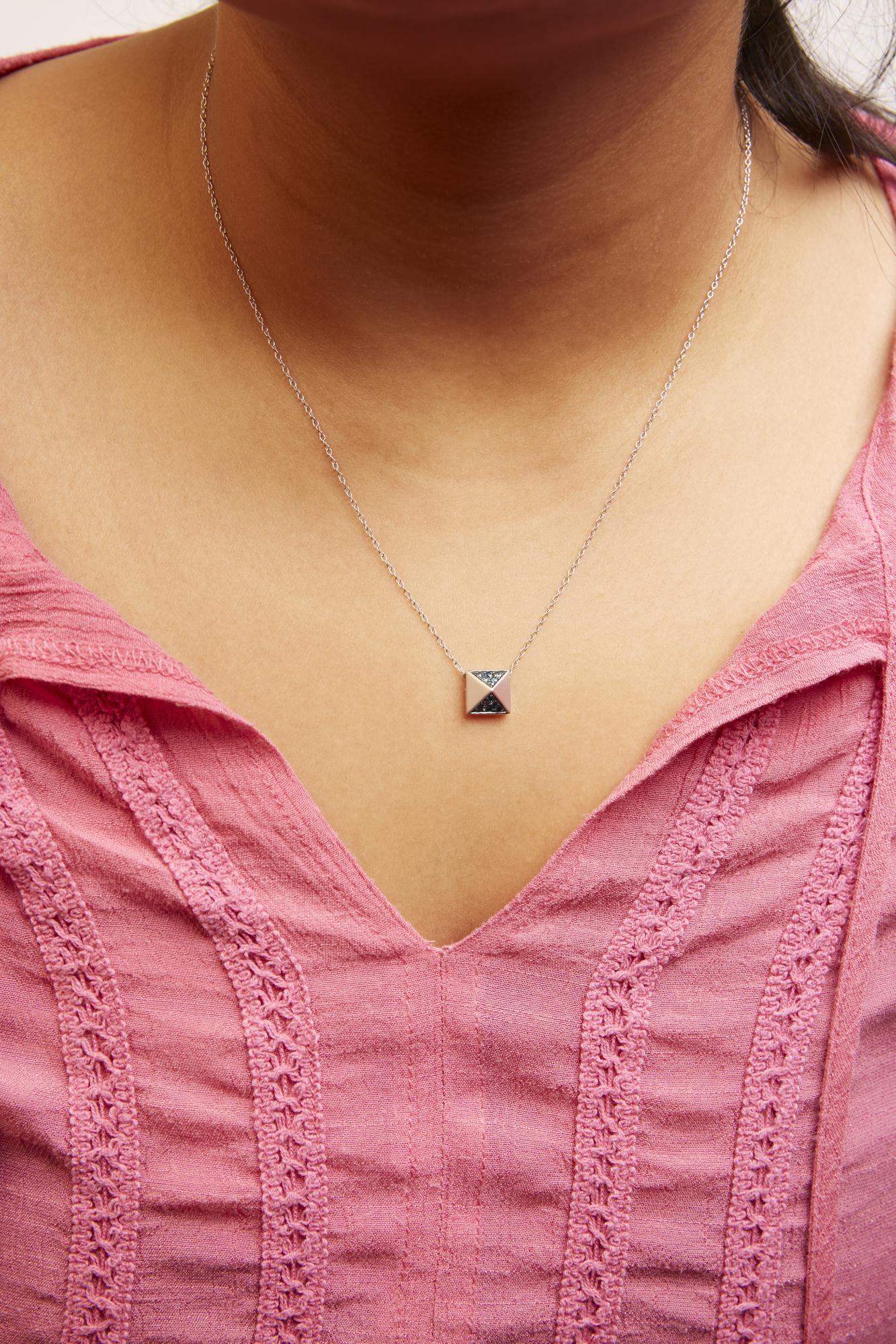 White necklace with a square pendant featuring sections with blue gemstones in pave setting, shown worn on a model from a front close-up angle.