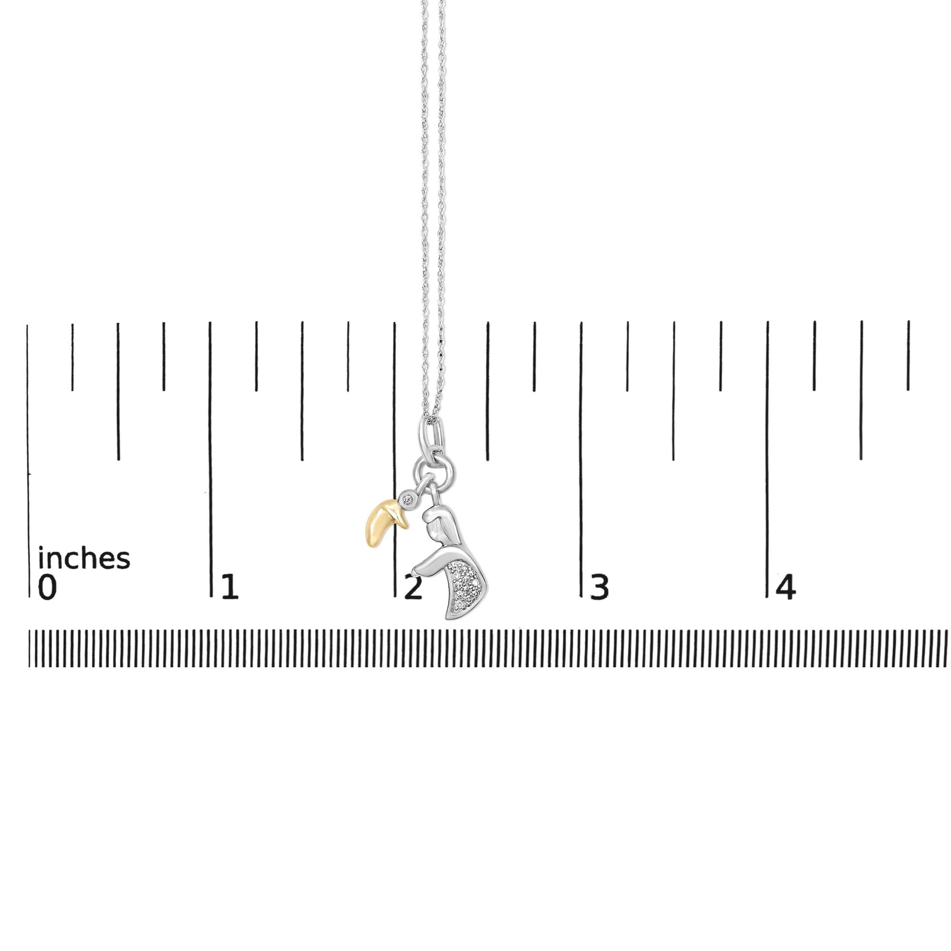 Necklace shown on a scale with a pendant, featuring a yellow metal curved charm, a silver metal hand-shaped charm with white gemstones in pave setting, and a small round white gemstone in bezel setting, front view.