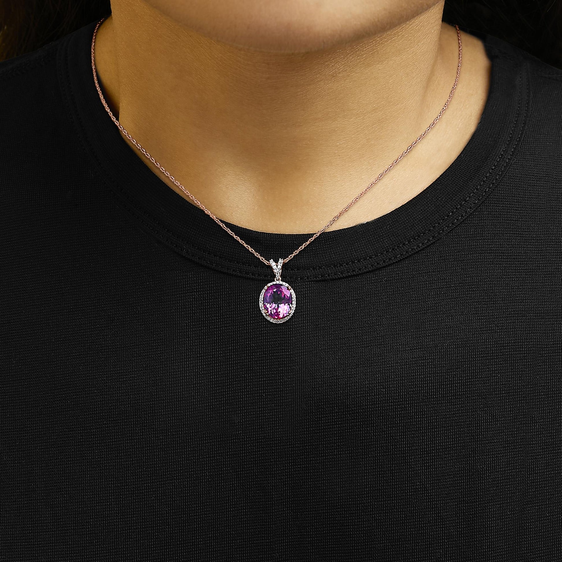 Close-up front view of a rose metal necklace with an oval pink gemstone pendant surrounded by small white gemstones, shown worn on a model.
