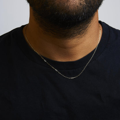 Close-up front view of a model wearing a thin yellow metal chain necklace with elongated rectangular links, styled over a black shirt.
