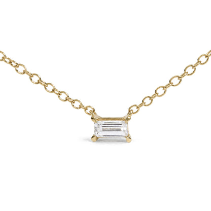 Close-up front view of a yellow metal necklace with a baguette-shaped white gemstone in a prong setting on a chain with oval links against a white background.