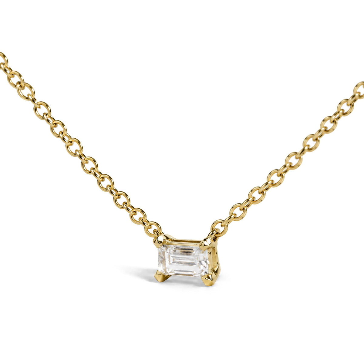 Close-up front angle of a yellow metal necklace chain with a single white baguette-shaped gemstone pendant in prong setting.