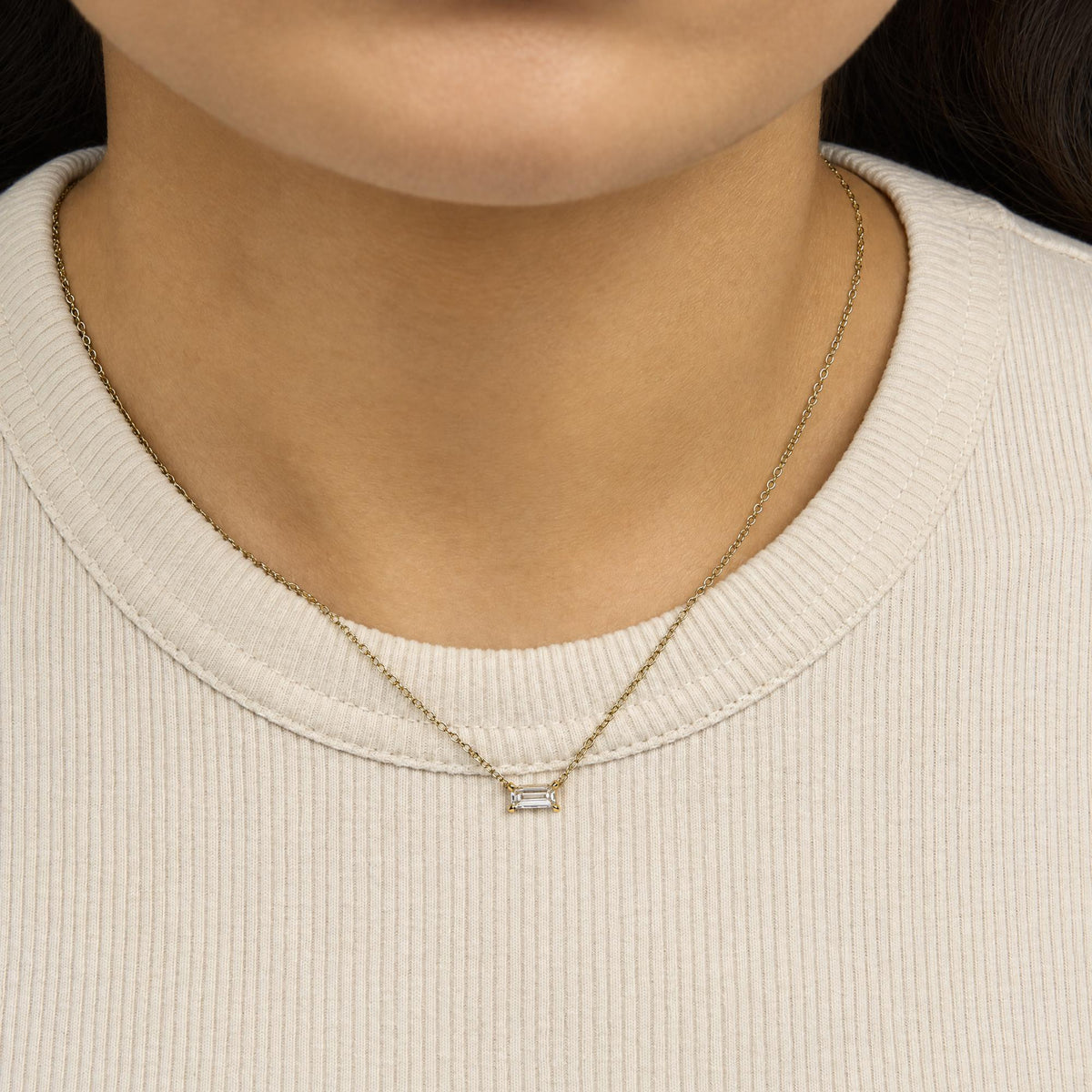 Yellow metal necklace with a single white baguette gemstone pendant in prong setting, shown worn on a model, close-up front angle.