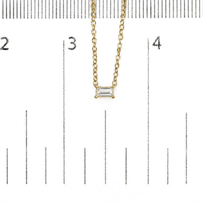 Close-up shot of a yellow metal chain necklace with a rectangular white gemstone pendant in a prong setting, shown on a measurement scale.