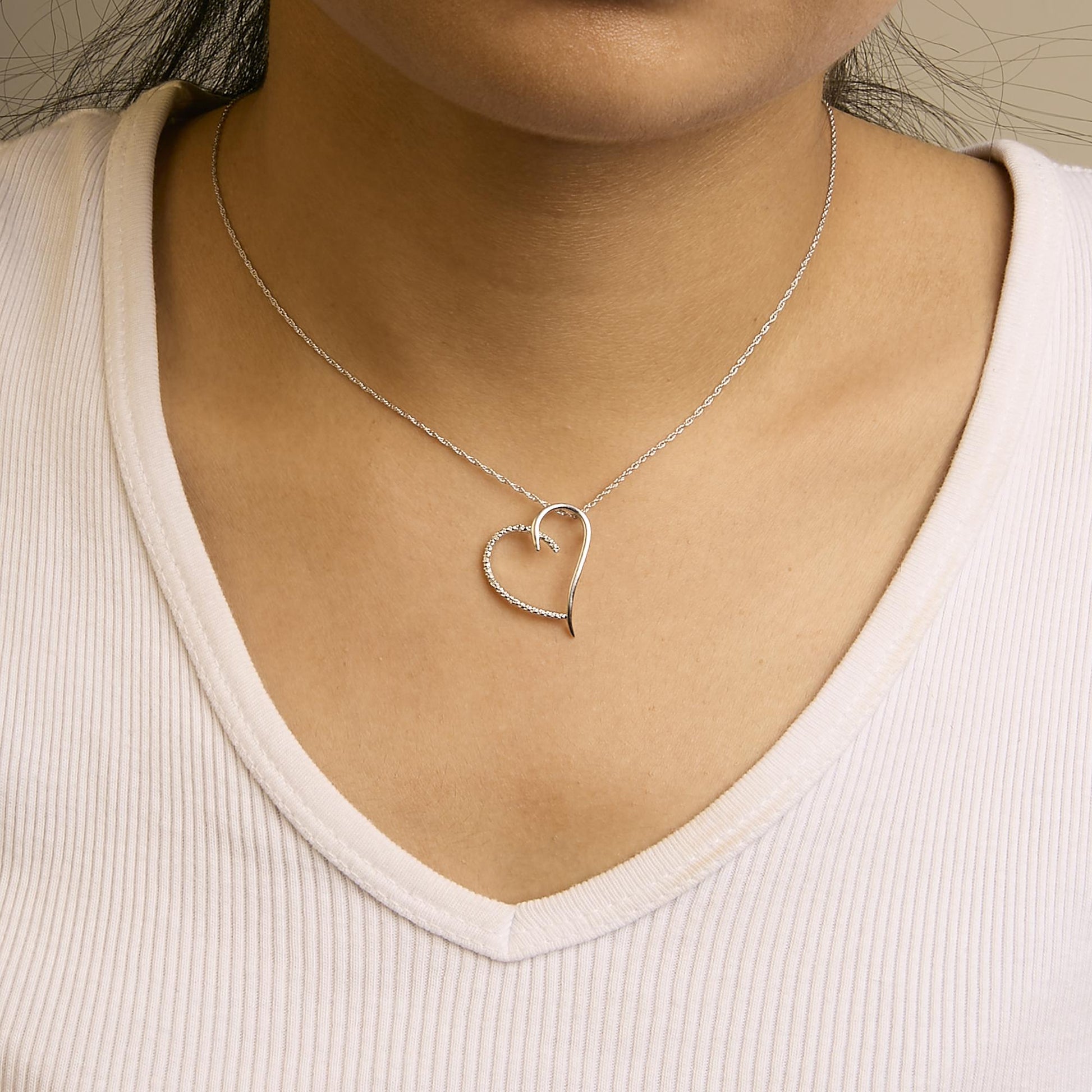 Necklace in white metal with an open heart-shaped pendant, one half plain and the other half adorned with round white gemstones, shown on a model from the front angle.