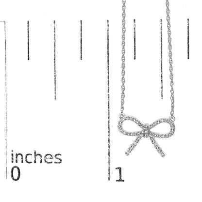 Close-up front angle of a white necklace with a bow-shaped pendant adorned with small round white gemstones in prong settings, shown on a scale marked in inches.
