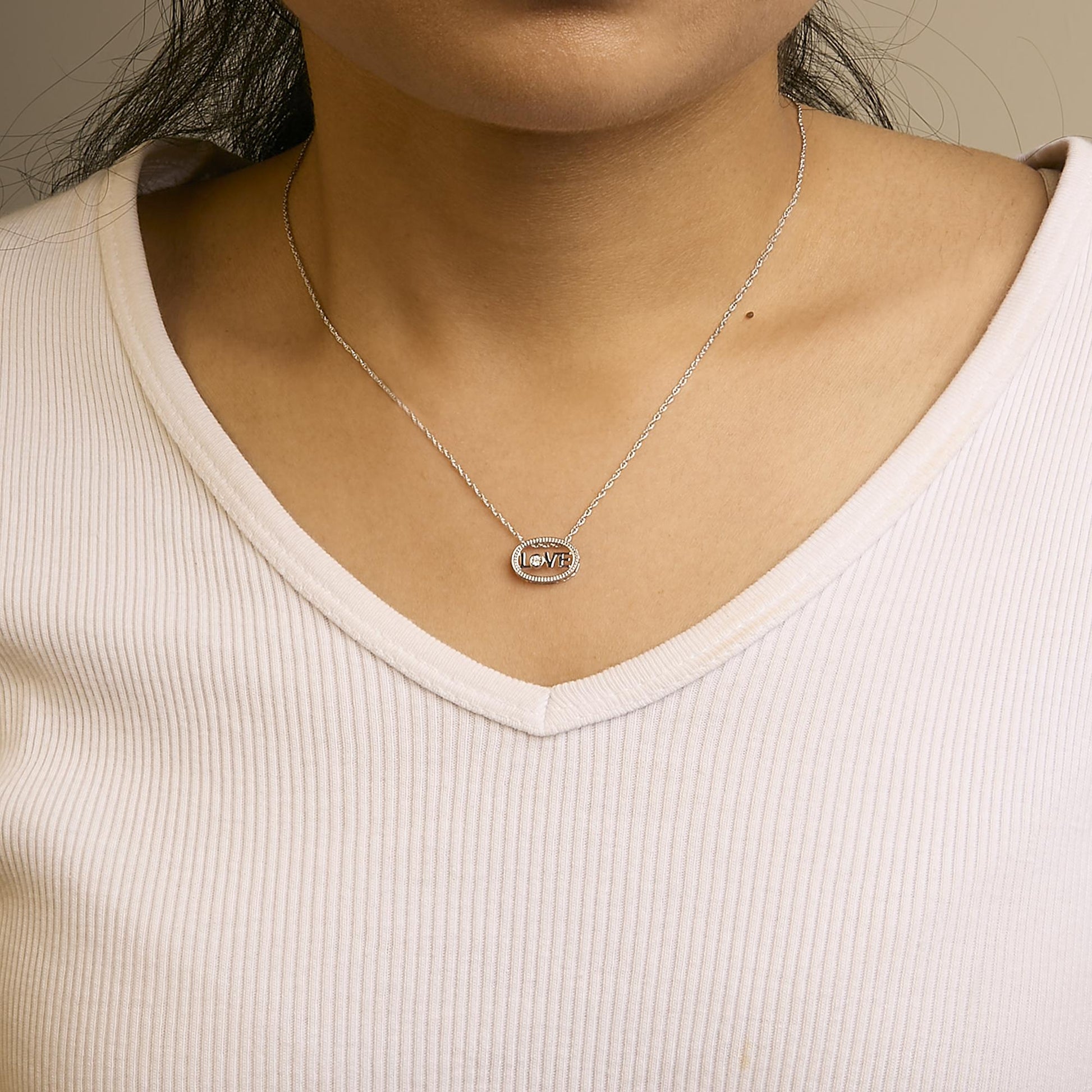 Front view of a white metal necklace on a model featuring an oval pendant with the word 'LOVE' and a single round white gemstone in a prong setting.