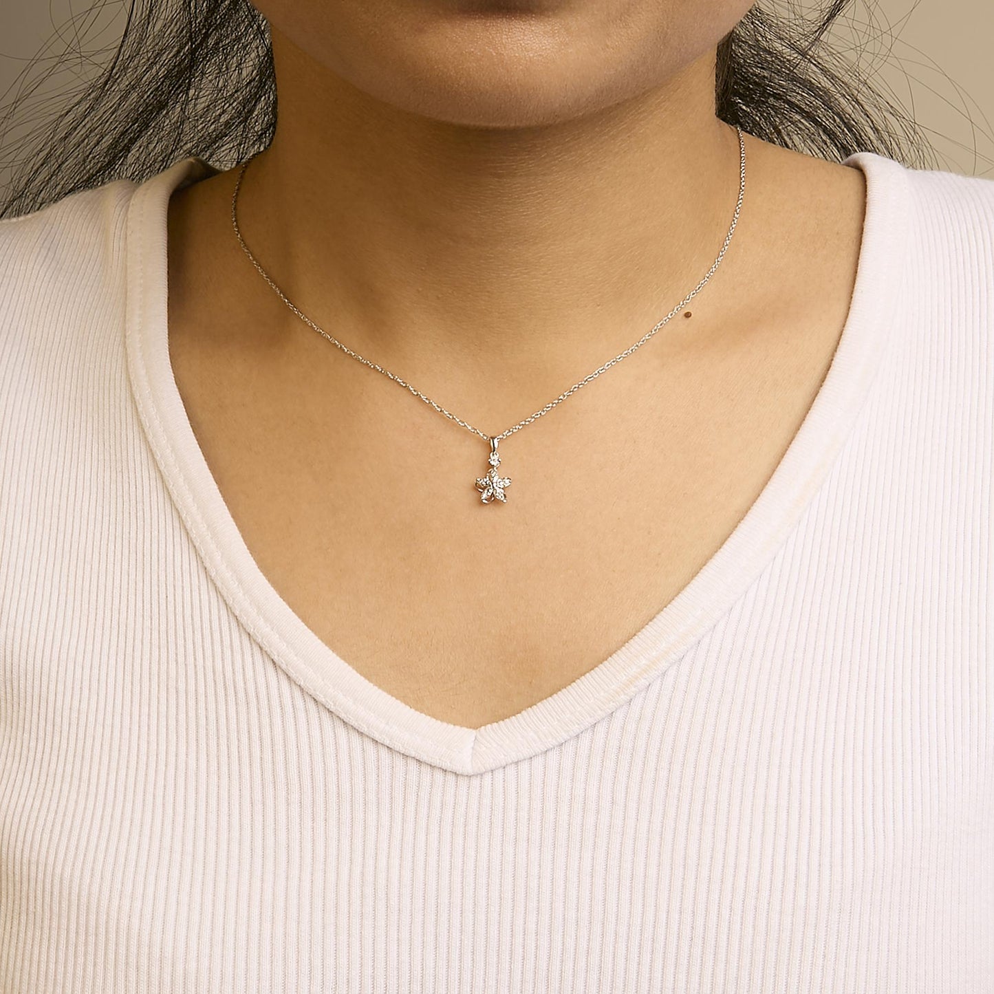 Close-up front view of a white metal necklace on a model, featuring a pendant with round white gemstones in prong settings.