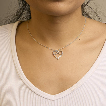 Front view of a white metal necklace on a model, featuring a heart-shaped pendant with an infinity symbol adorned with round white gemstones in prong settings.