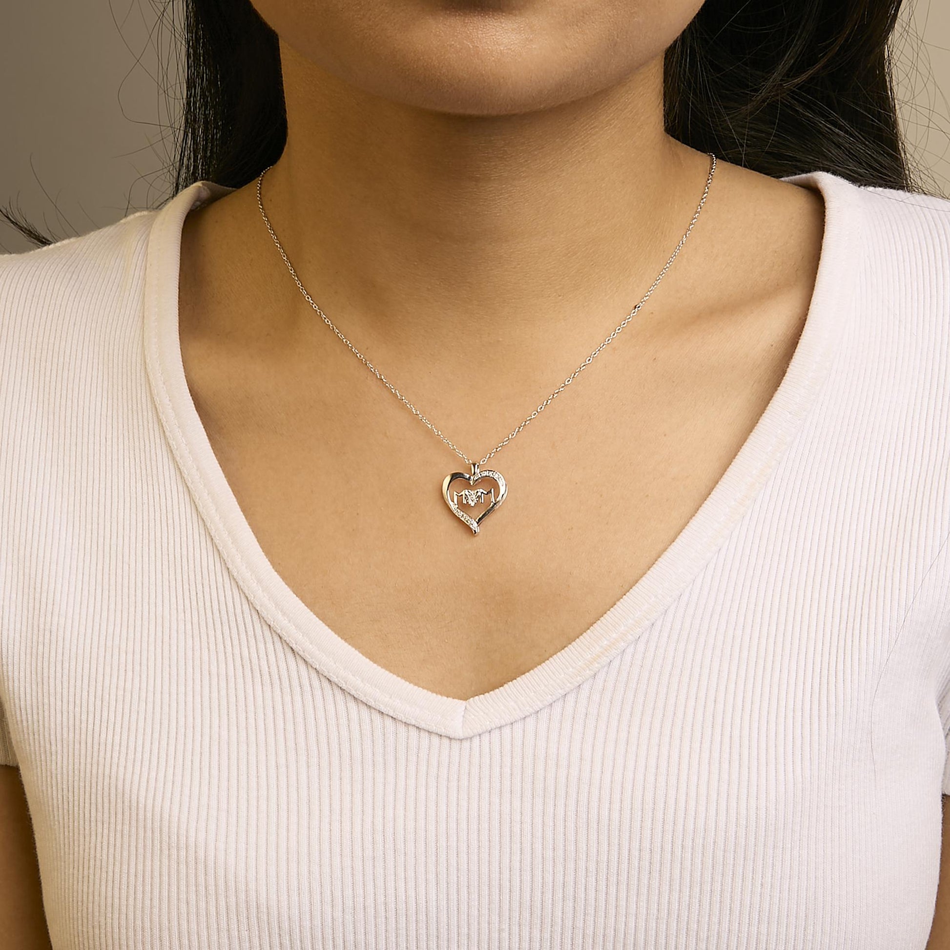 Close-up front view of a white metal heart-shaped necklace with five round white gemstones in prong settings, worn on a model with a white ribbed V-neck top.