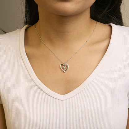 Close-up front view of a white metal heart-shaped necklace with five round white gemstones in prong settings, worn on a model with a white ribbed V-neck top.