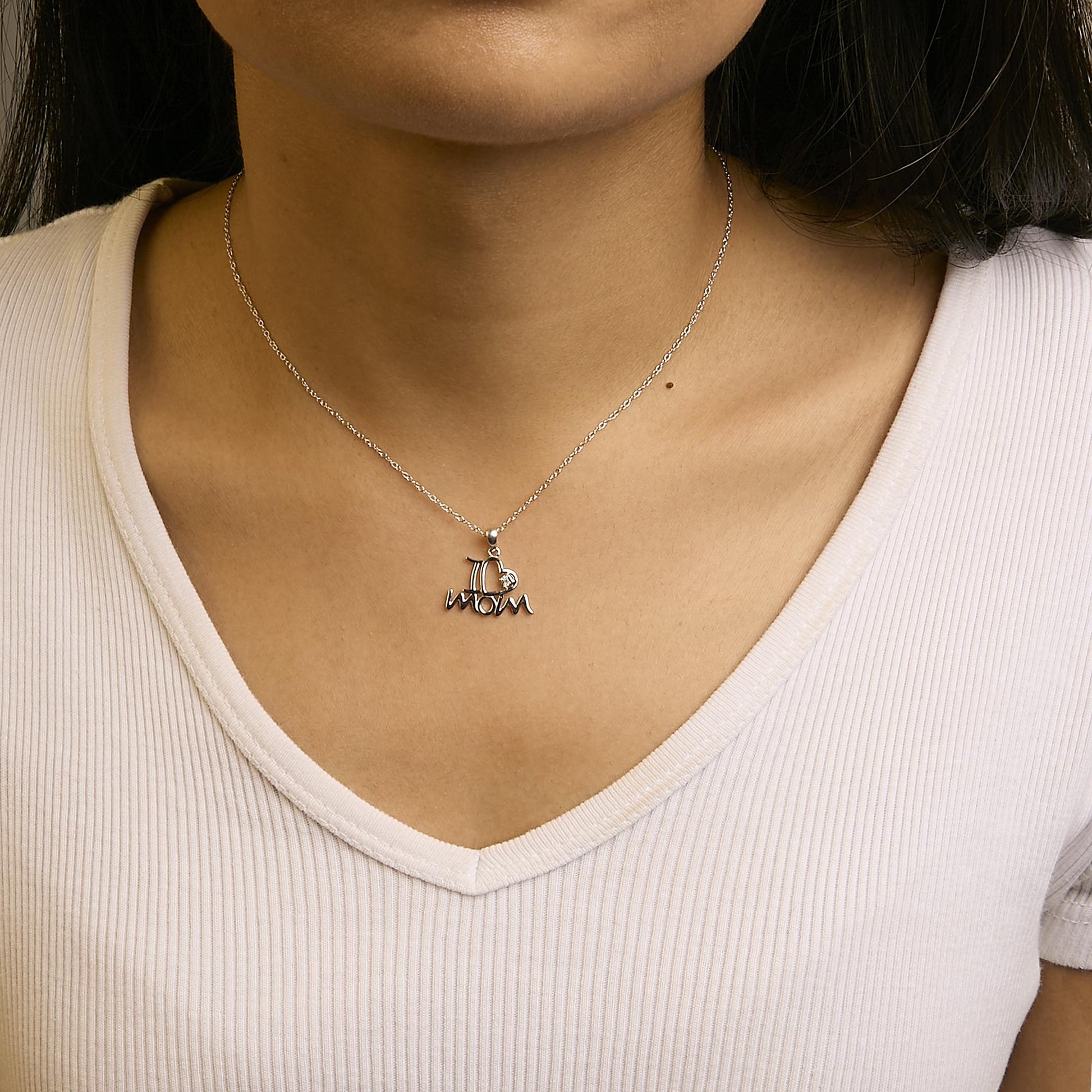 Close-up front view of a white metal necklace on a model with a pendant spelling 'mom' and featuring one round white gemstone in a prong setting.