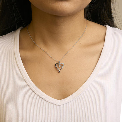 White metal heart-shaped necklace pendant with five round white gemstones in prong settings, worn on a model, front view.