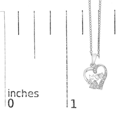 White metal heart-shaped necklace pendant with the word 'Mom' inside, adorned with white gemstones, shown hanging on a chain, photographed against a ruler for size reference.