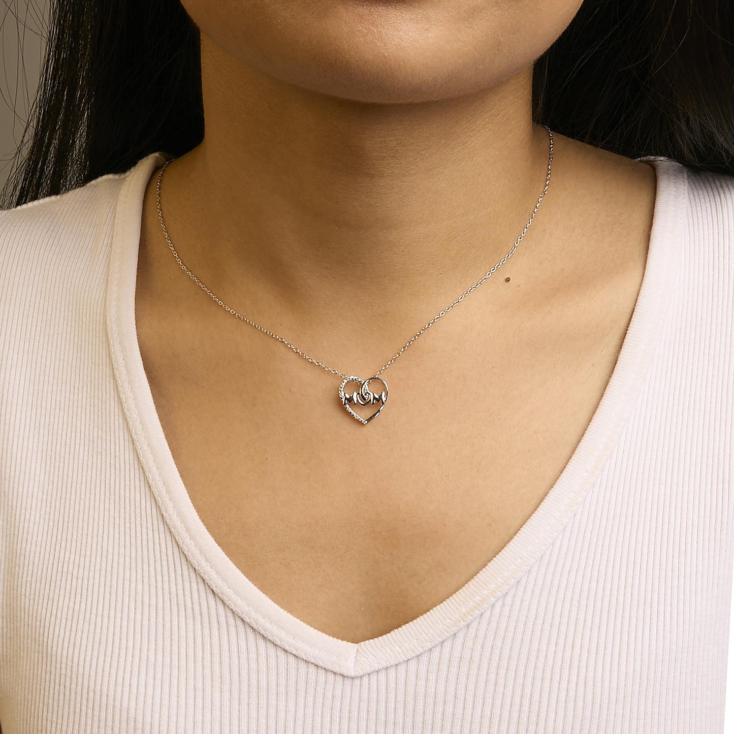 Close-up front view of a white metal necklace with a heart-shaped pendant featuring white round gemstones in prong settings, worn on a model.