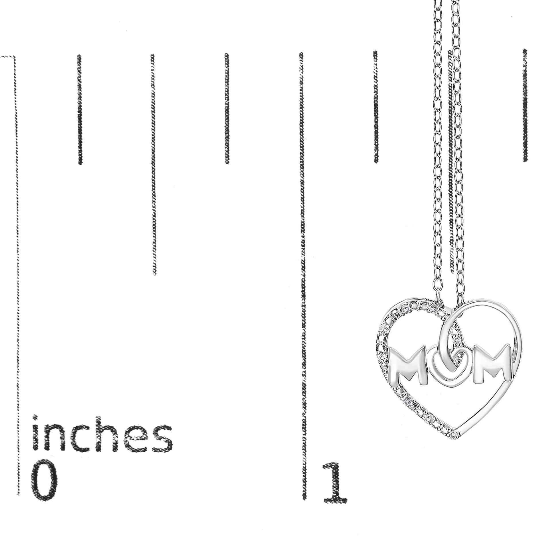 Close-up front angle of a white metal necklace pendant with the word 'MOM' inside a heart shape adorned with round white gemstones in prong settings, shown on a ruler for size reference.