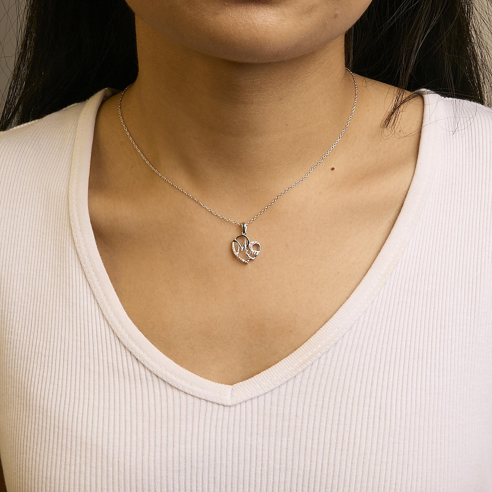 White metal necklace with a heart-shaped pendant featuring round white gemstones in a prong setting, worn on a model, front angle.