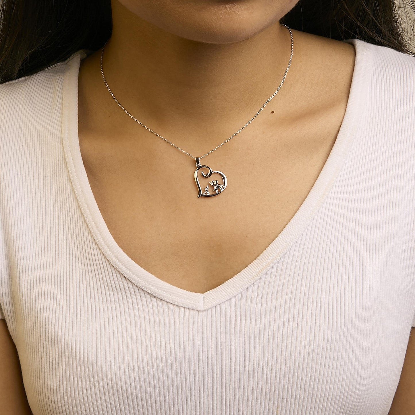Close-up front view of a model wearing a white metal necklace with an open heart-shaped pendant featuring four round white gemstones in prong settings.