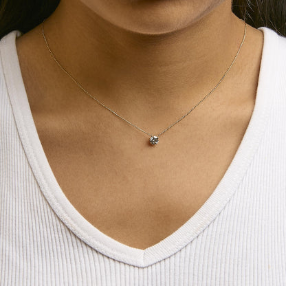 Close-up front view of a yellow metal necklace with a single round white gemstone in a 4-prong setting, worn on a model with a white top.