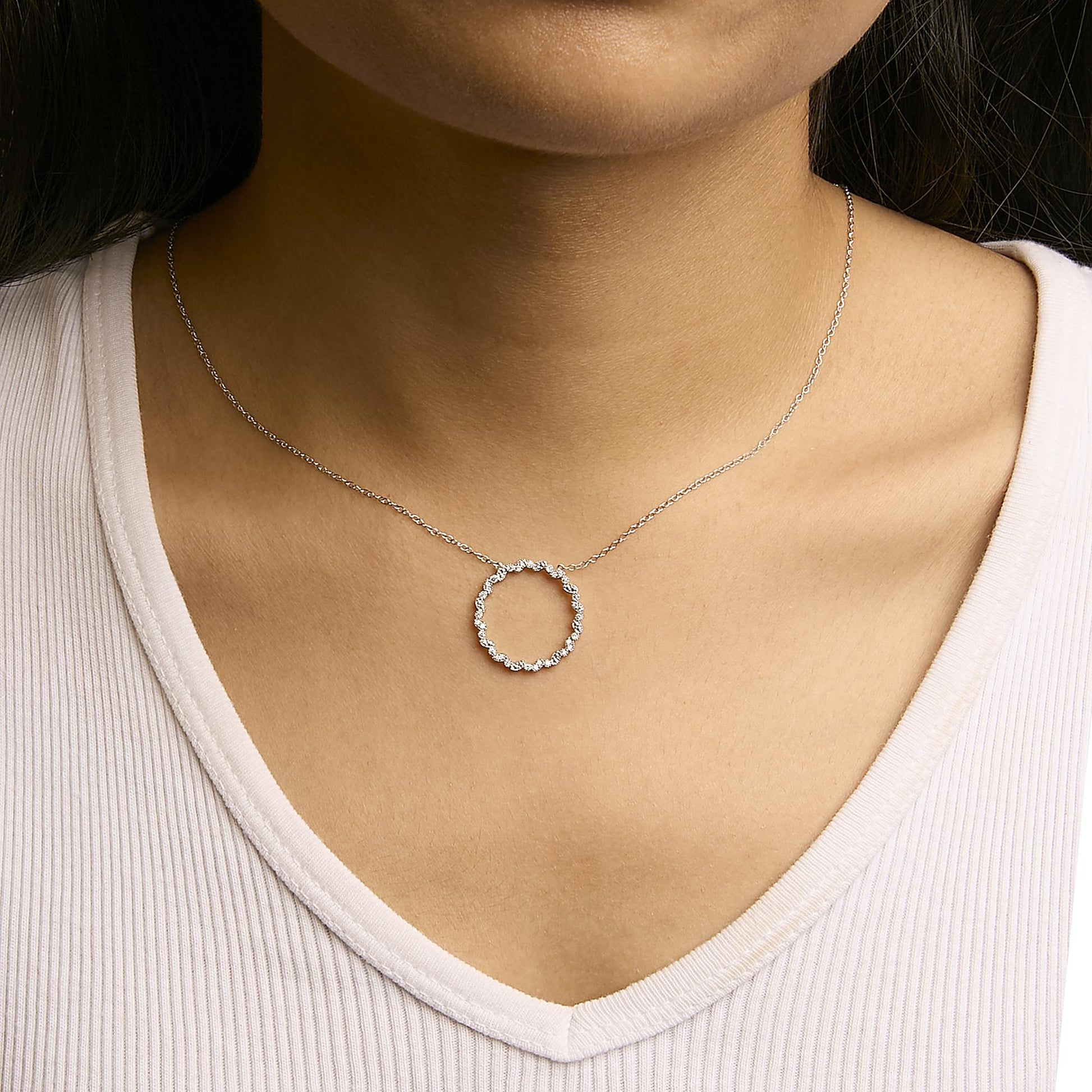 White metal necklace with a circular pendant of round white gemstones in prong settings, shown on a model from a front-angle close-up.
