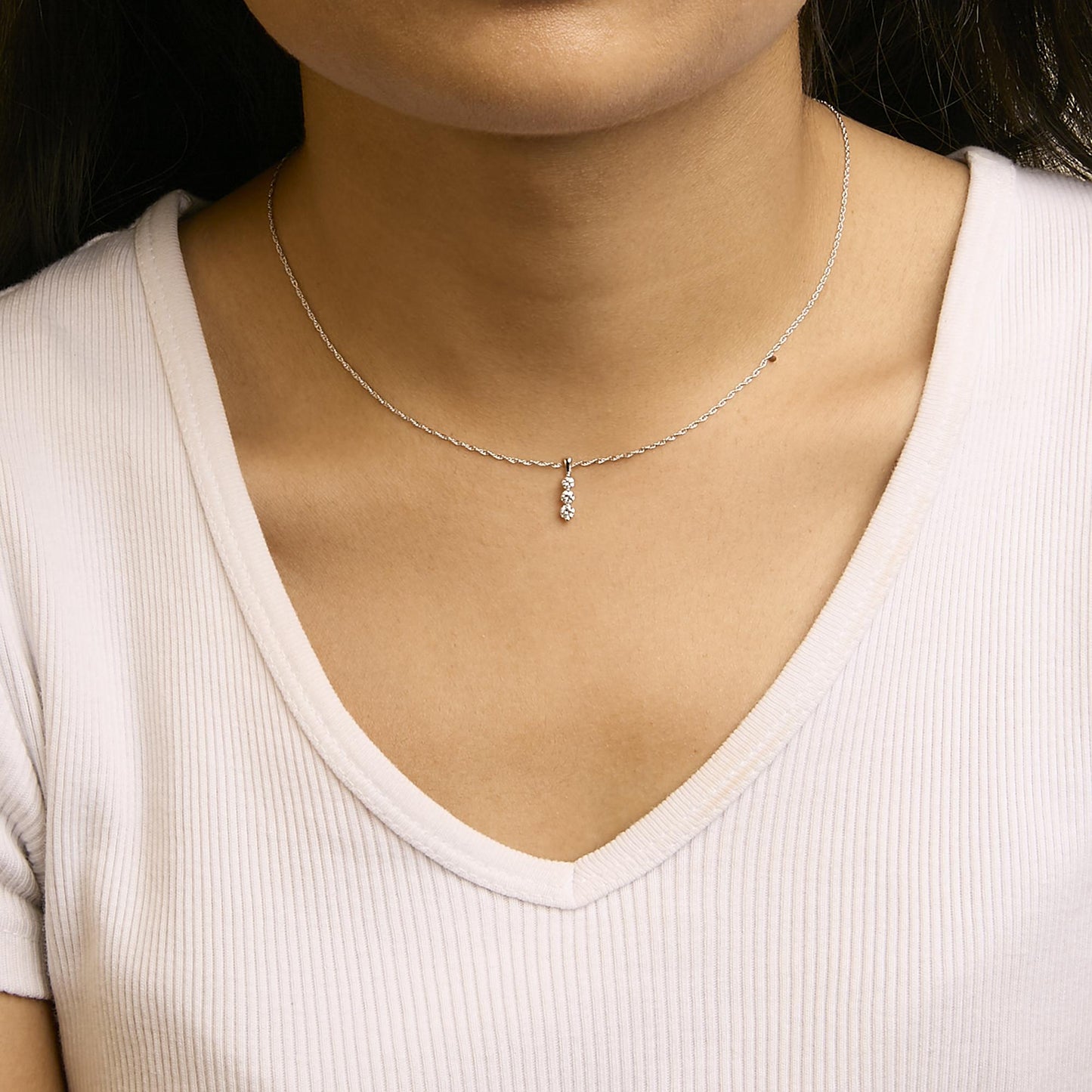 Close-up front view of a white metal necklace with a pendant featuring three round white gemstones in prong settings, worn on a model.