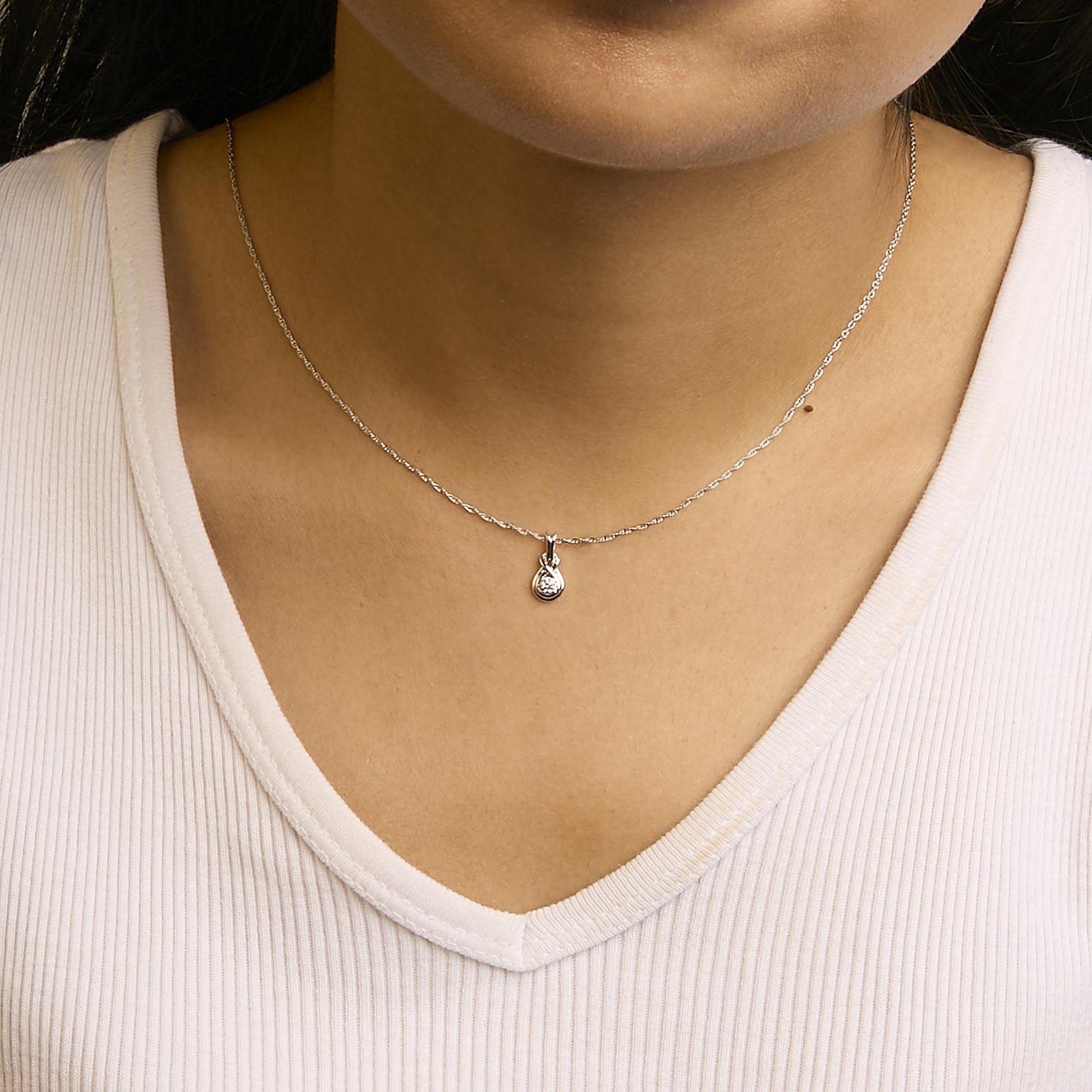 Close-up front view of a white metal necklace with a small round pendant featuring a single white gemstone, worn on a model.