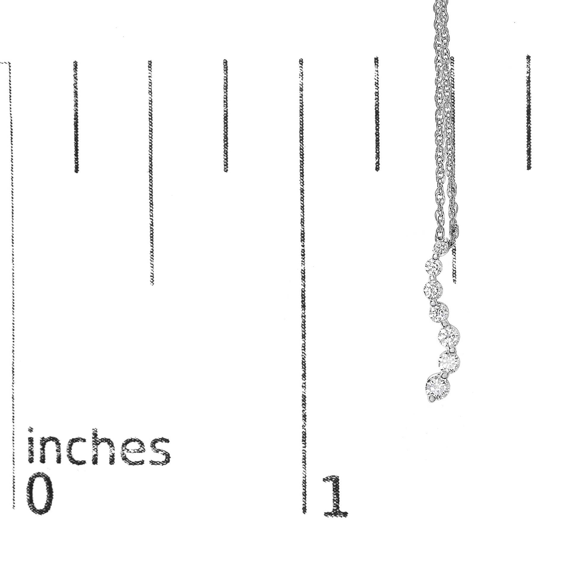 White metal necklace with a pendant of seven round white gemstones in prong settings, displayed vertically on a ruler for size reference, shot from the front.