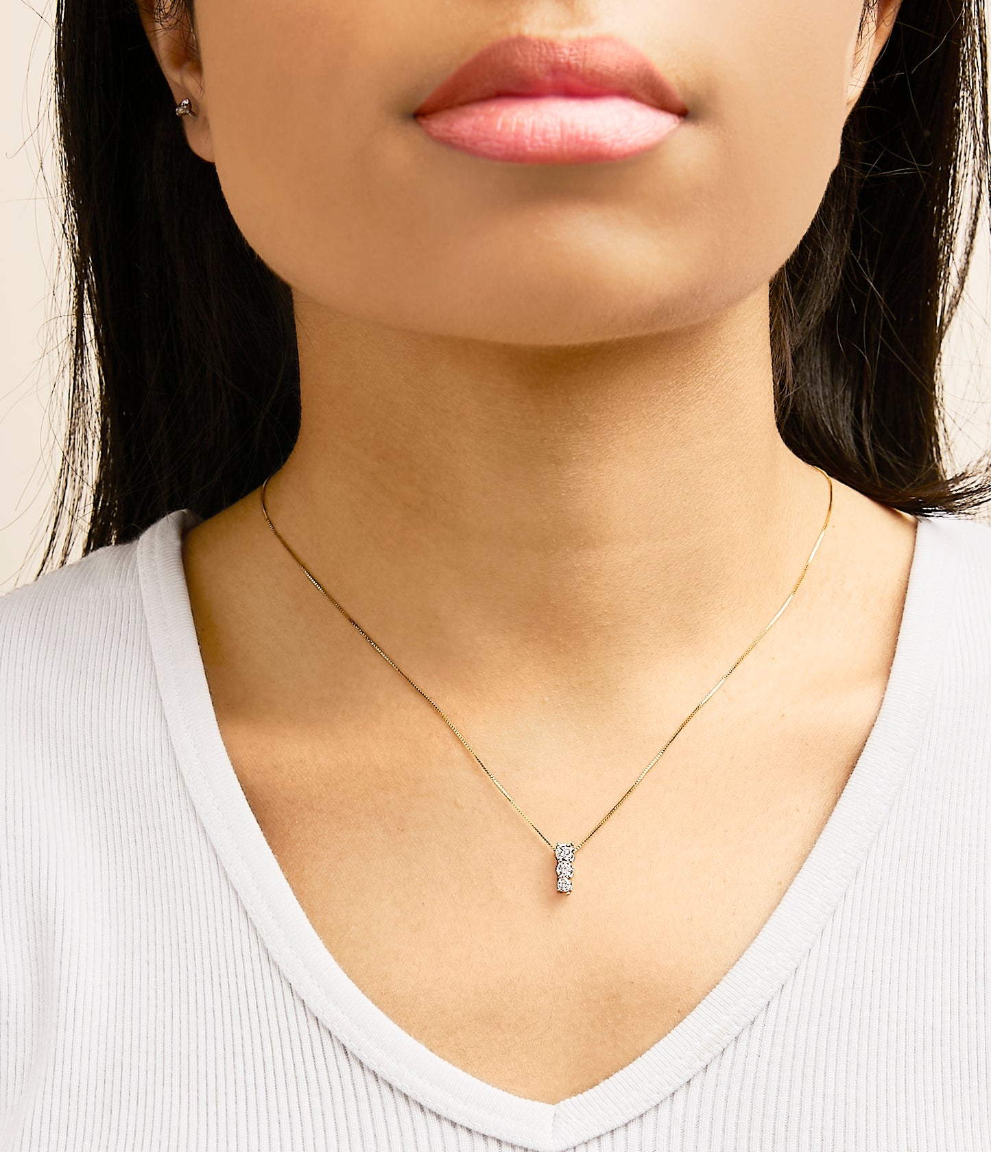 Close-up front view of a model wearing a yellow metal necklace with a vertical pendant set with three round white gemstones in a shared prong setting.