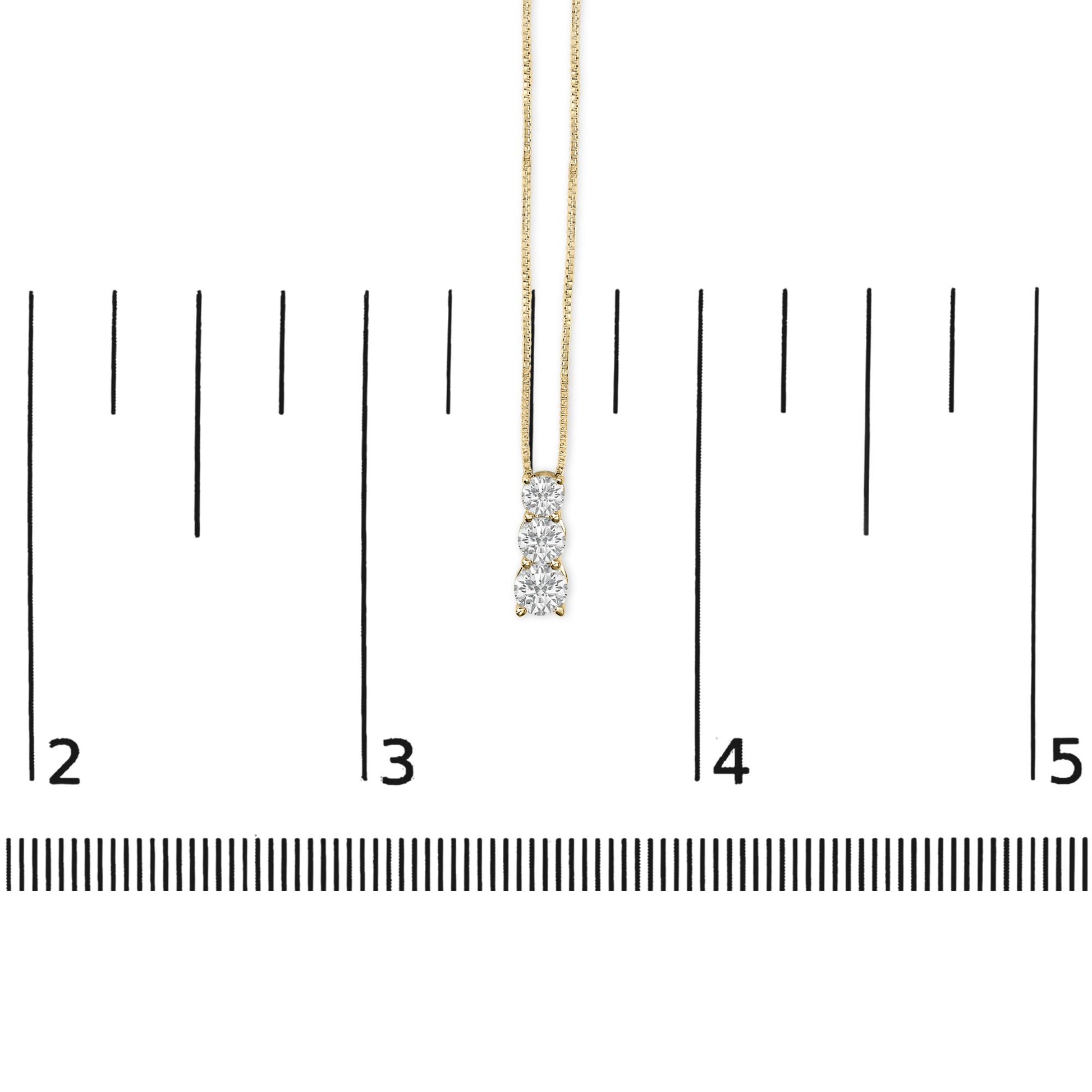 Yellow metal necklace with three vertically aligned round white gemstones in shared prong setting, shown on a measuring scale, front view.