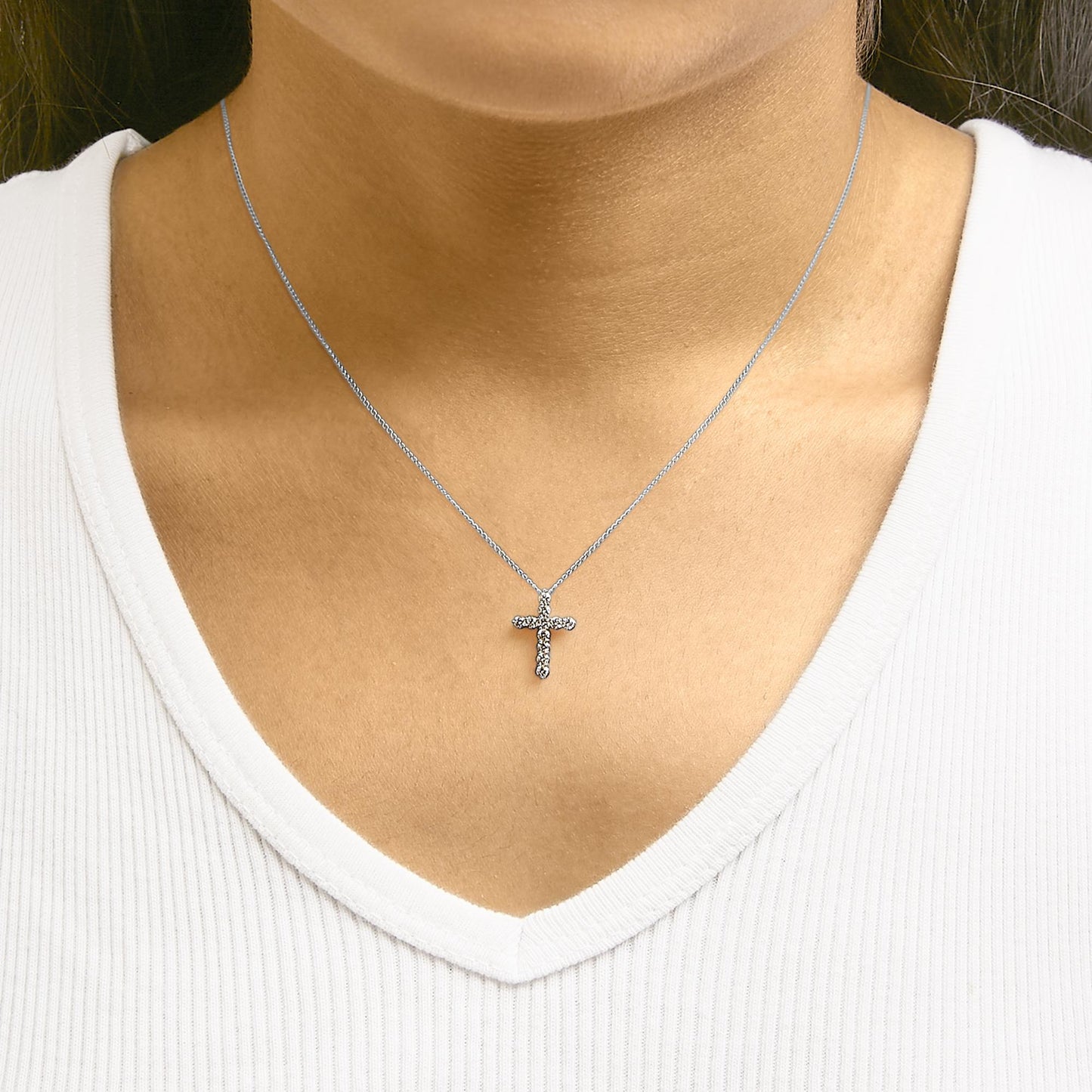 Close-up front view of a white necklace with a cross-shaped pendant featuring round white gemstones in a shared prong setting, worn on a model.