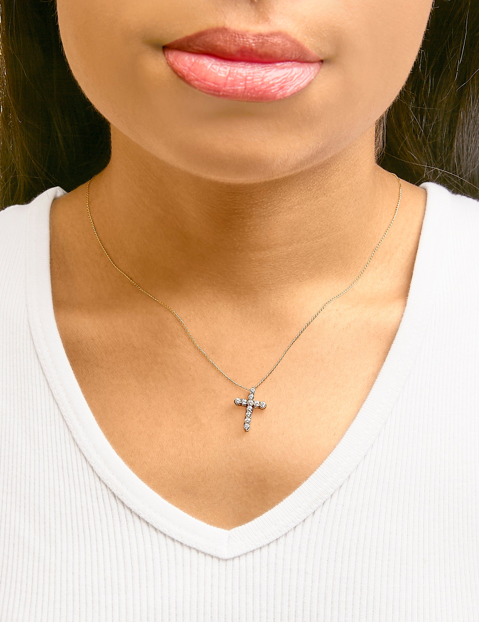 Necklace with yellow chain featuring a cross-shaped pendant set with round white gemstones, shown worn on a model from a front angle.