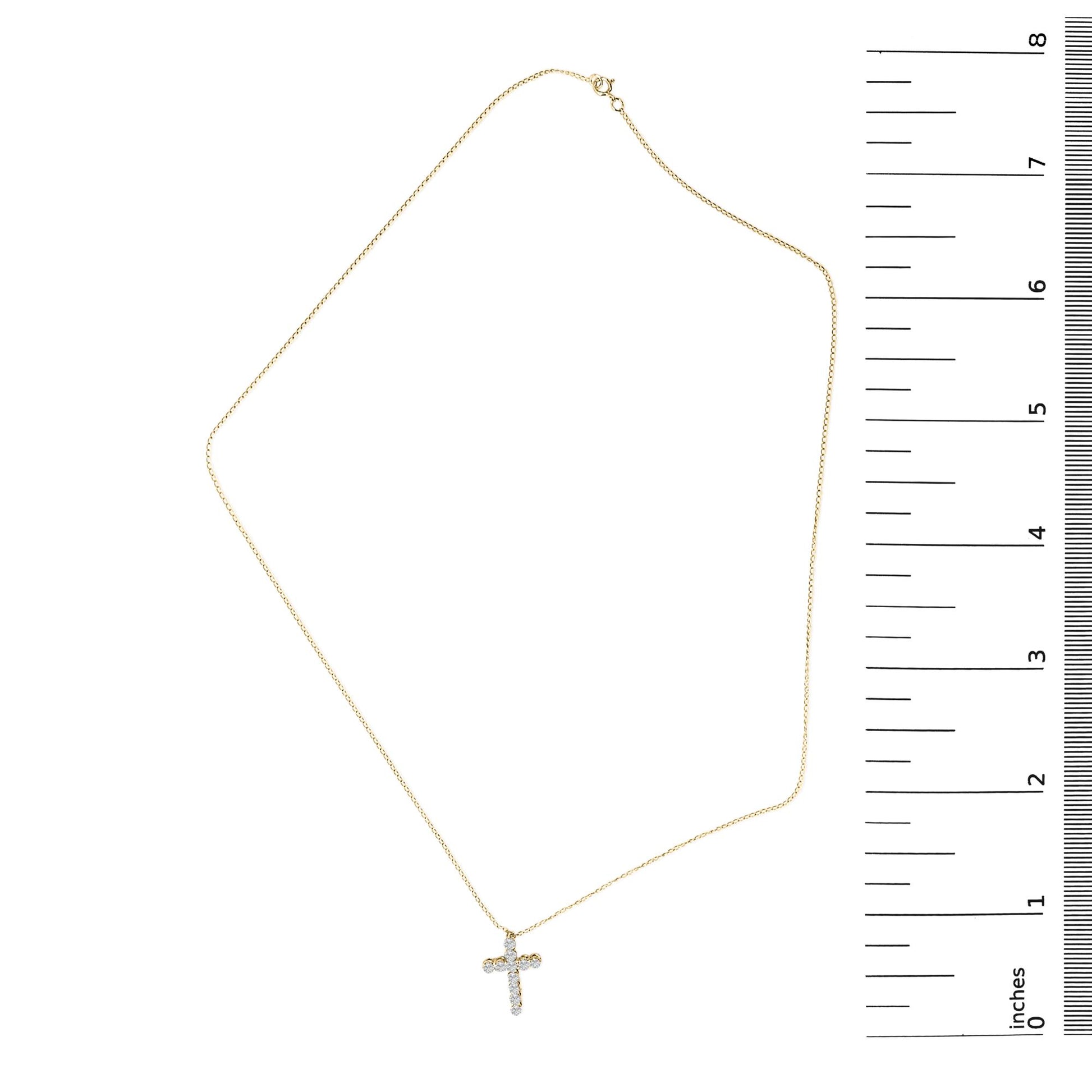 Yellow necklace with a small cross pendant set with round white gemstones in shared prong settings, shown laying flat next to a ruler for scale, image taken from above.