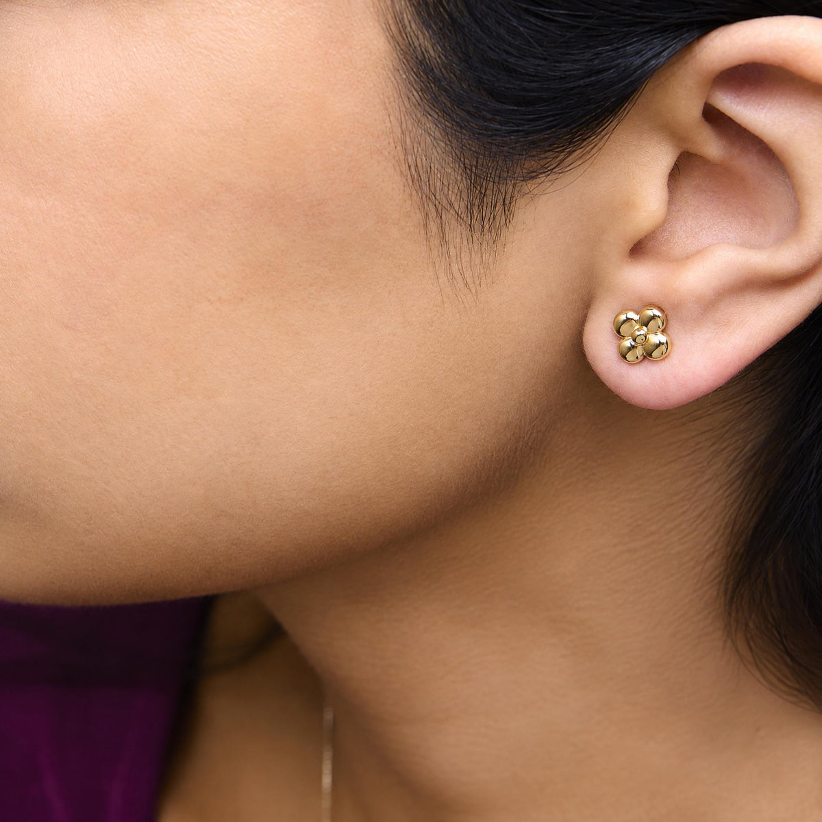Close-up side view of a model wearing yellow metal flower-shaped stud earrings.