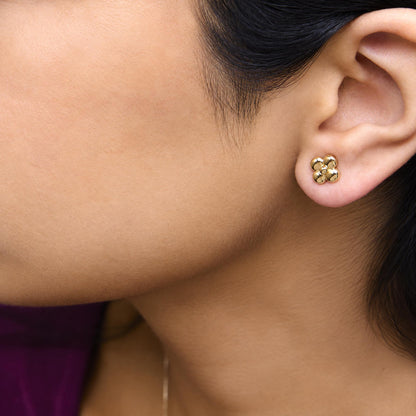 Close-up side view of a model wearing yellow metal flower-shaped stud earrings.