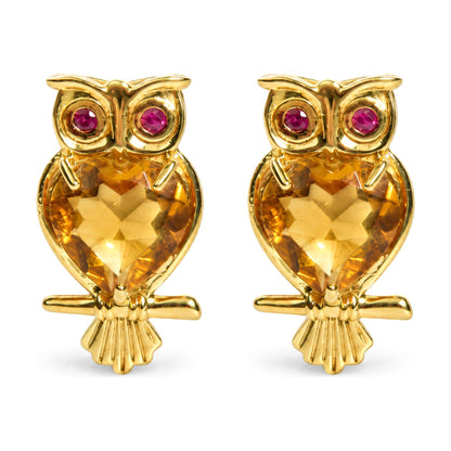 Close-up front view of owl-shaped yellow metal earrings with heart-shaped yellow gemstones as the body and round red gemstones as the eyes, shown on a white background.
