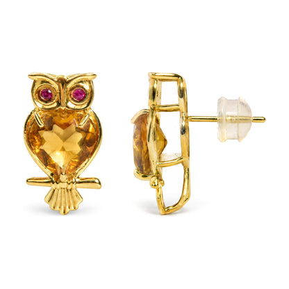Close-up front and side view of yellow metal owl-shaped earrings with heart-shaped yellow gemstones and round red gemstones, shown on a white background.