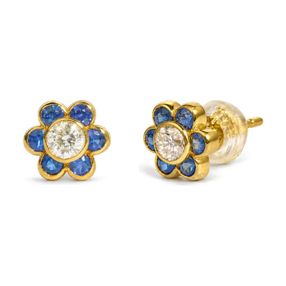 Close-up front and side view of yellow metal flower-shaped stud earrings with a round white gemstone in the center and round blue gemstones surrounding it, shown on a white background.