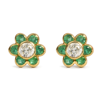 Close-up front angle of a pair of yellow metal flower-shaped earrings with round white gemstones in the center and round green gemstones forming the petals, shown on a white background.