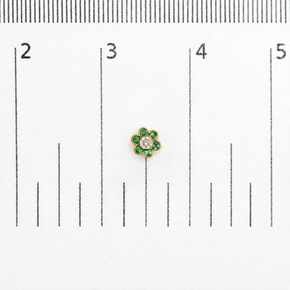 Close-up top view of a single yellow metal flower-shaped earring with round green gemstones forming petals and a round white gemstone in the center, shown on a scale background.